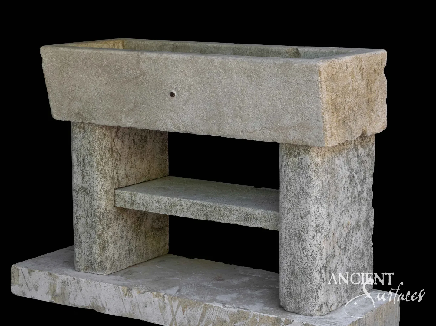 Plain deep reclaimed limestone trough sink on two thick slab legs with a lower stone shelf, the legs mottled grey green with lichen