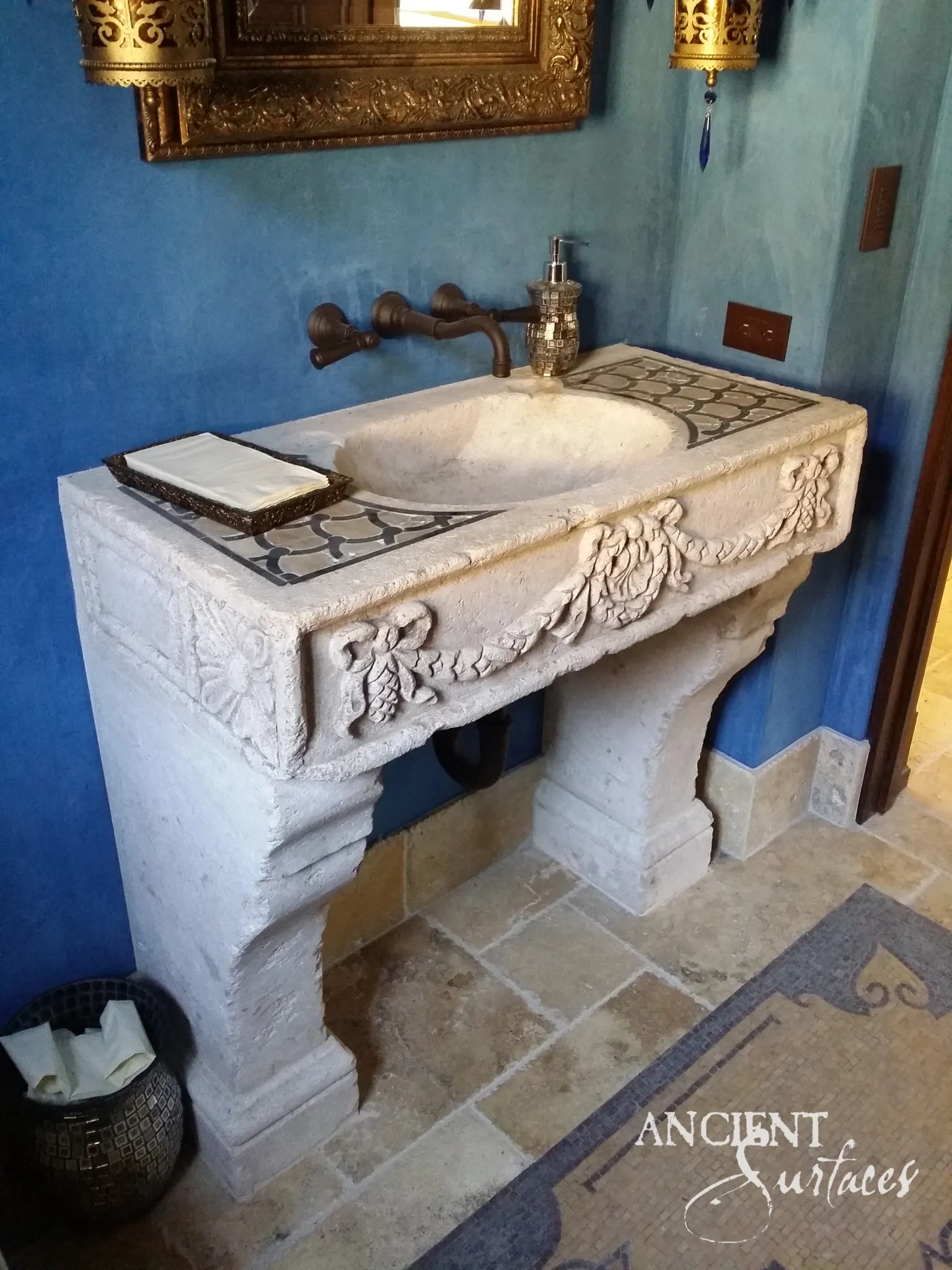 Hand carved limestone console sink in a blue powder room, with ribbon bow garlands on the apron, fish scale mosaic beside the oval bowl and curved scroll legs