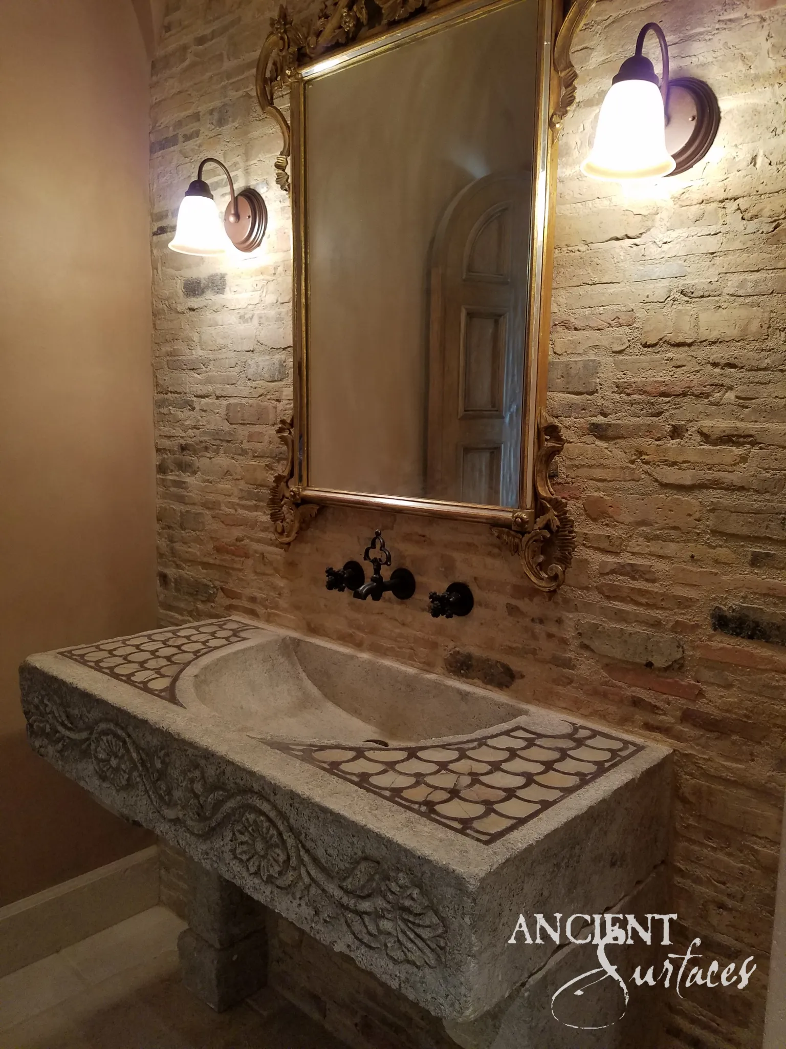 Reclaimed limestone trough sink installed against exposed brick, with a long sloping bowl, fish scale mosaic inlay at both ends and a scrolling vine carved along the front