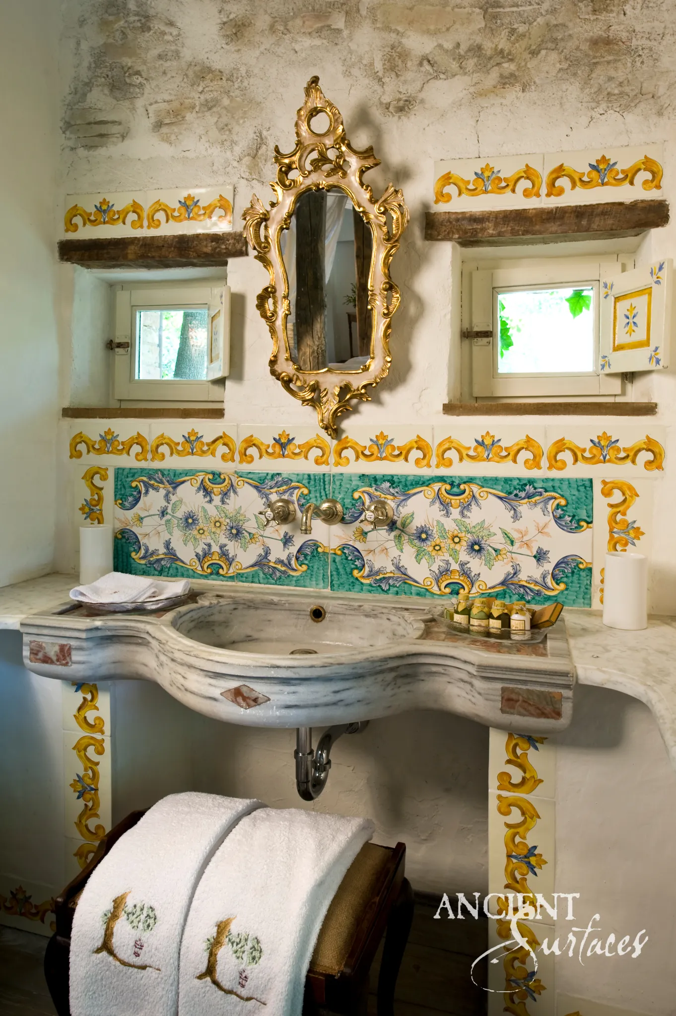 Serpentine front reclaimed limestone sink with inlaid rose and ochre lozenges on its front edge, a rounded bowl and drain, installed beneath a painted tile splash