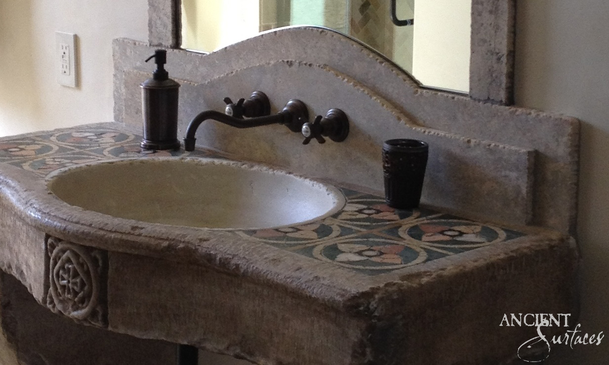 Installed reclaimed limestone sink with a bowed front, oval bowl, circular mosaic medallions on the top, a carved roundel on the apron and an arched stone backsplash