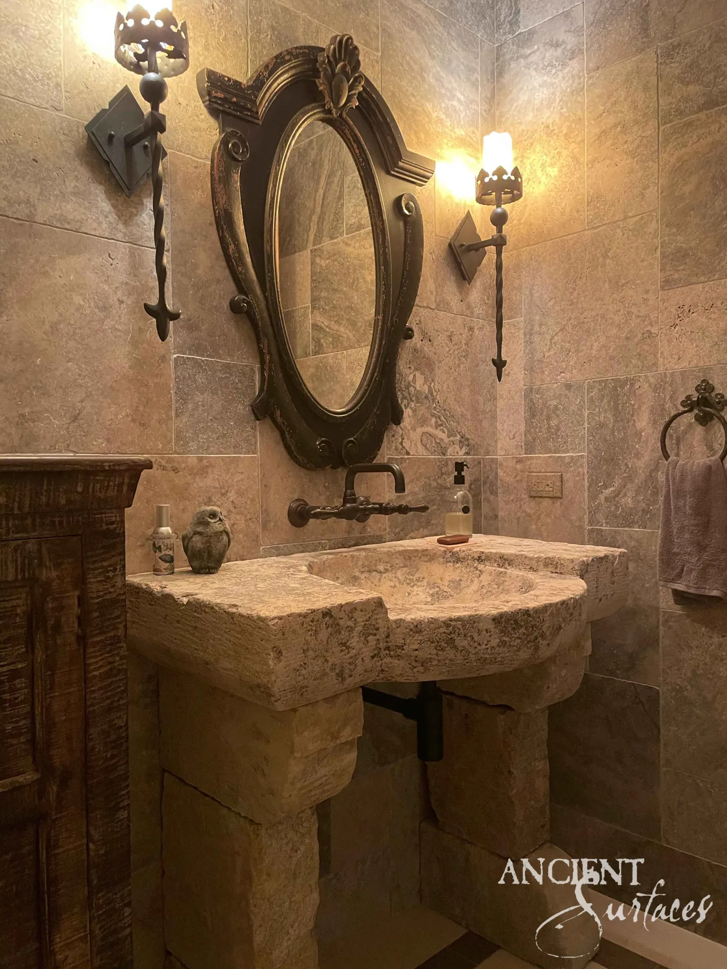 Rough hewn reclaimed limestone sink with a round bowl and curved front, resting on stacked limestone block piers in a stone tiled powder room