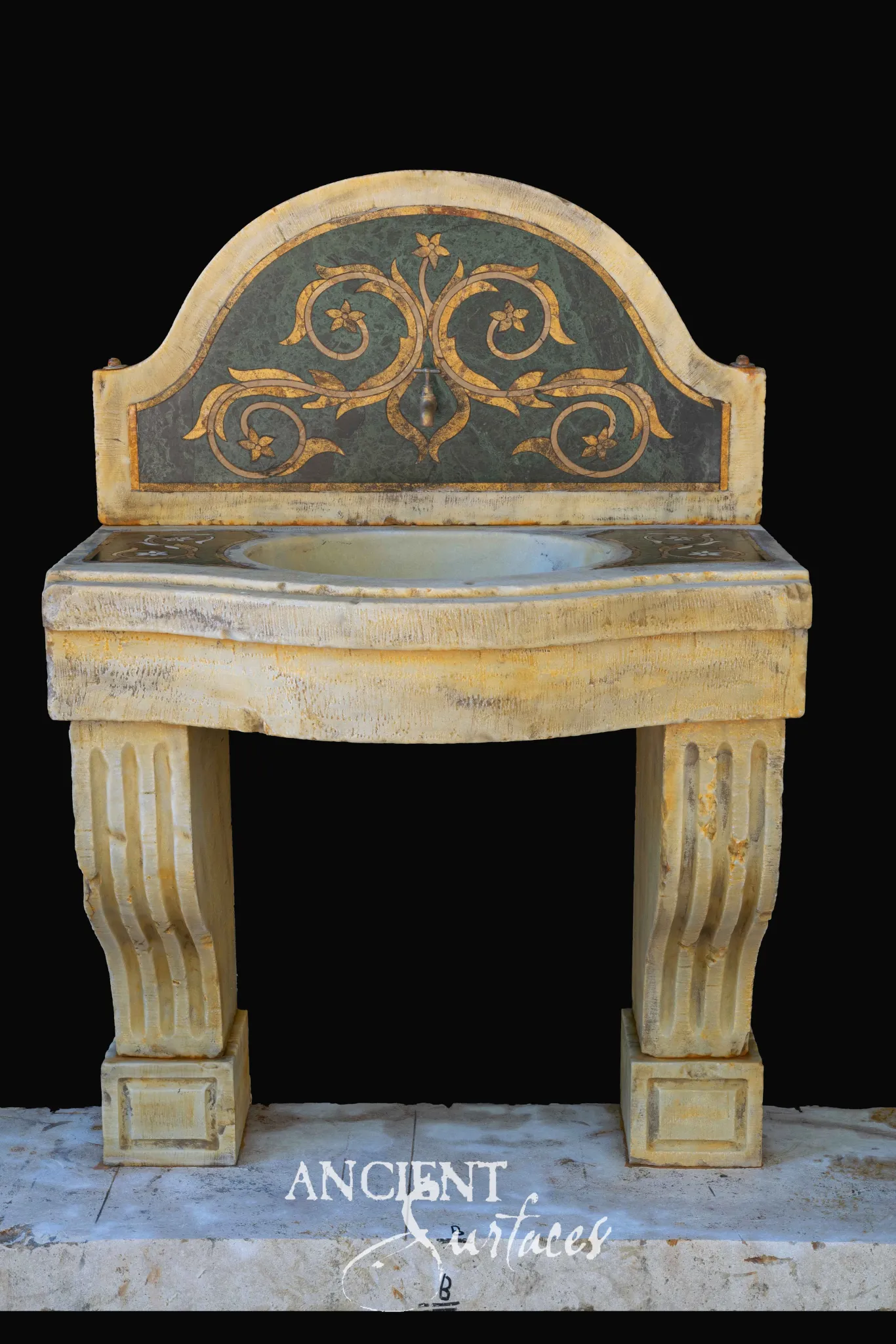 Reclaimed ochre limestone sink with an arched backsplash inlaid with green and gold scrolling foliage, a bowed front oval bowl and two fluted scroll legs on panelled plinths