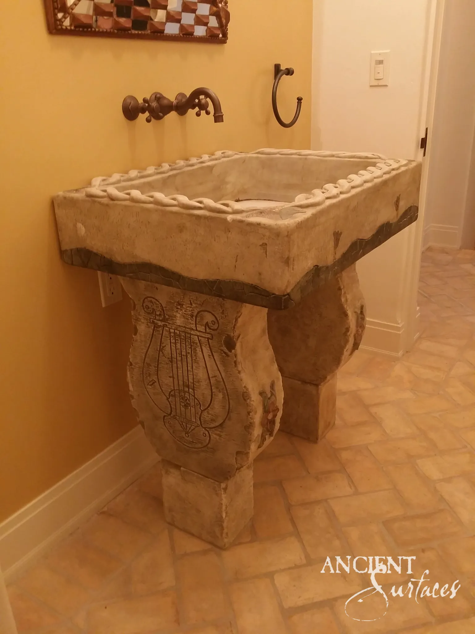 Reclaimed limestone sink with a carved twisted rope rim and a dark wavy band, set on two curved pedestal blocks, one incised with a lyre, in a powder room